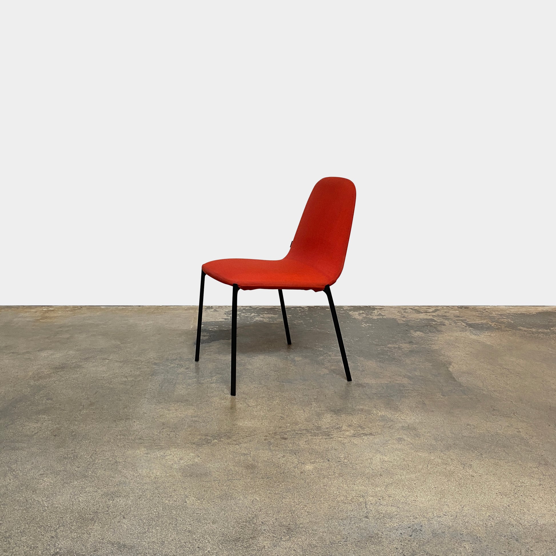 Four Zanotta Ella Dining Chairs, with their red fabric and black metal legs, are set in a row against a plain white background, showcasing the sleek design of this Italian brand.