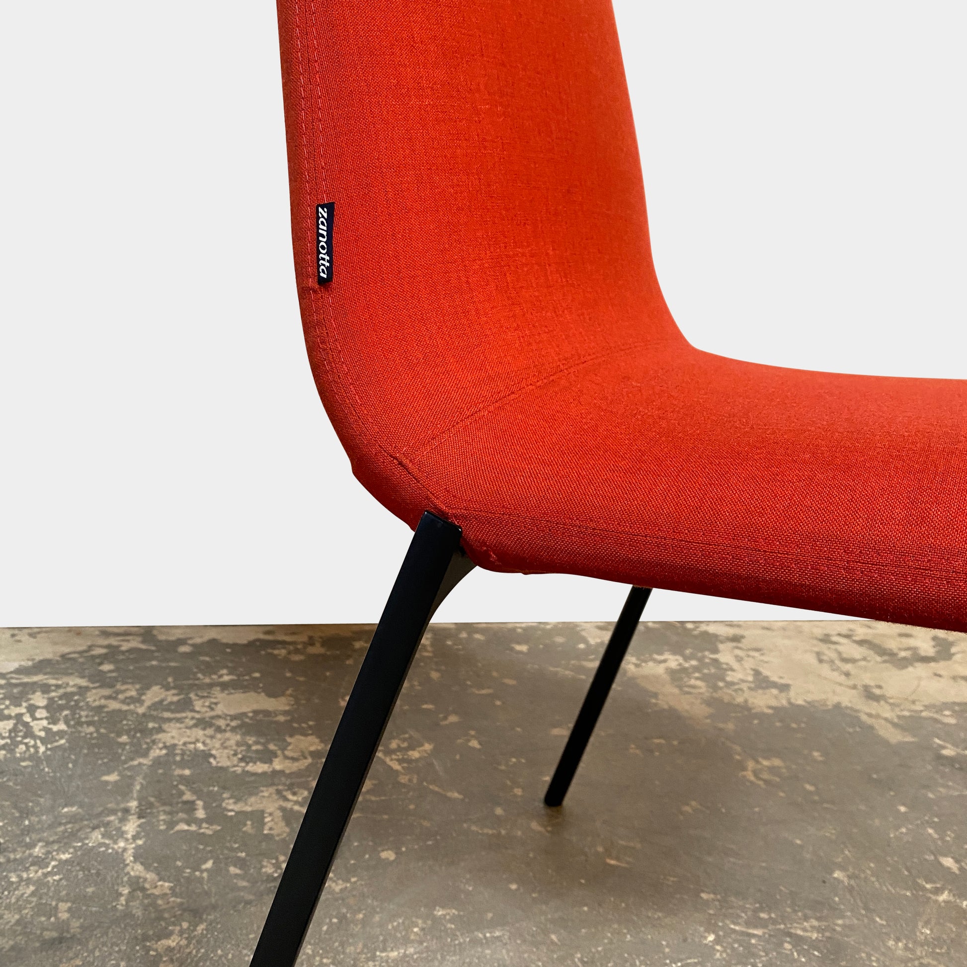 Four Zanotta Ella Dining Chairs, with their red fabric and black metal legs, are set in a row against a plain white background, showcasing the sleek design of this Italian brand.
