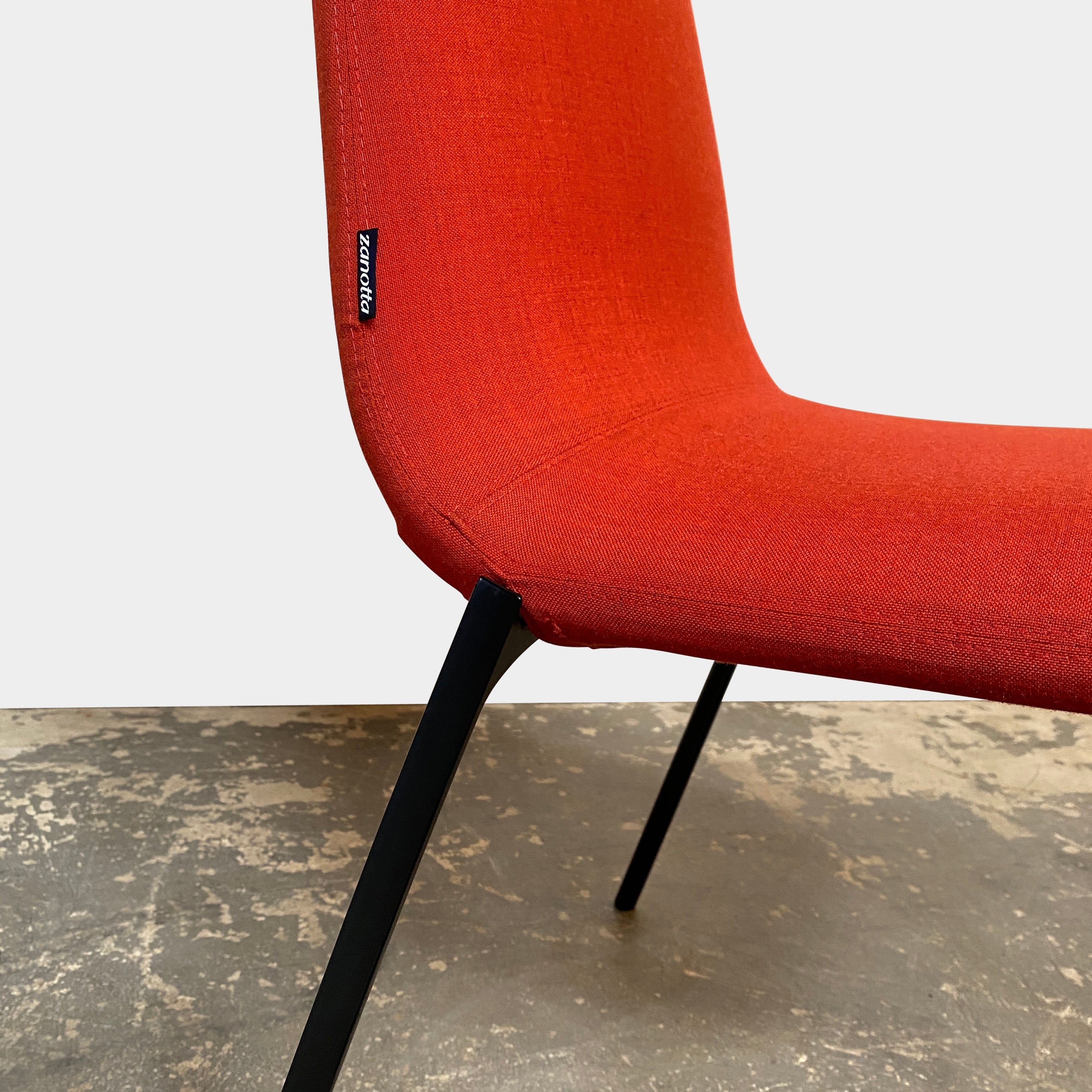 Four Zanotta Ella Dining Chairs, with their red fabric and black metal legs, are set in a row against a plain white background, showcasing the sleek design of this Italian brand.