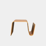The Offi Mag Table by Offi is a minimalist wooden side table with an angular, wave-inspired design. It serves as a multifunctional table or compact workstation, featuring a curved slot for storage—displayed on a plain white background.