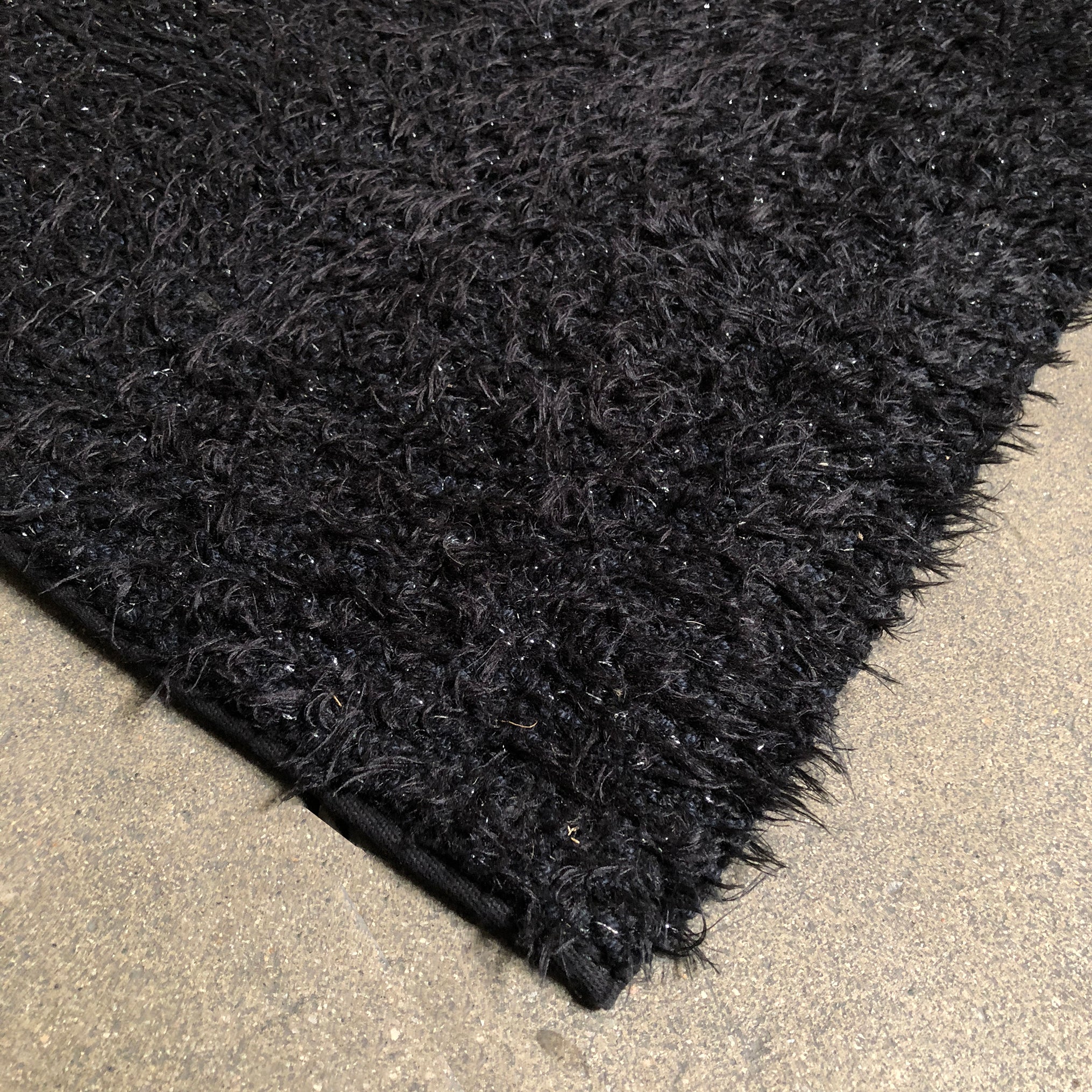 A close-up of the corner of a Kasthall Monroe Speckled Shag Rug on a plain, light-colored floor.