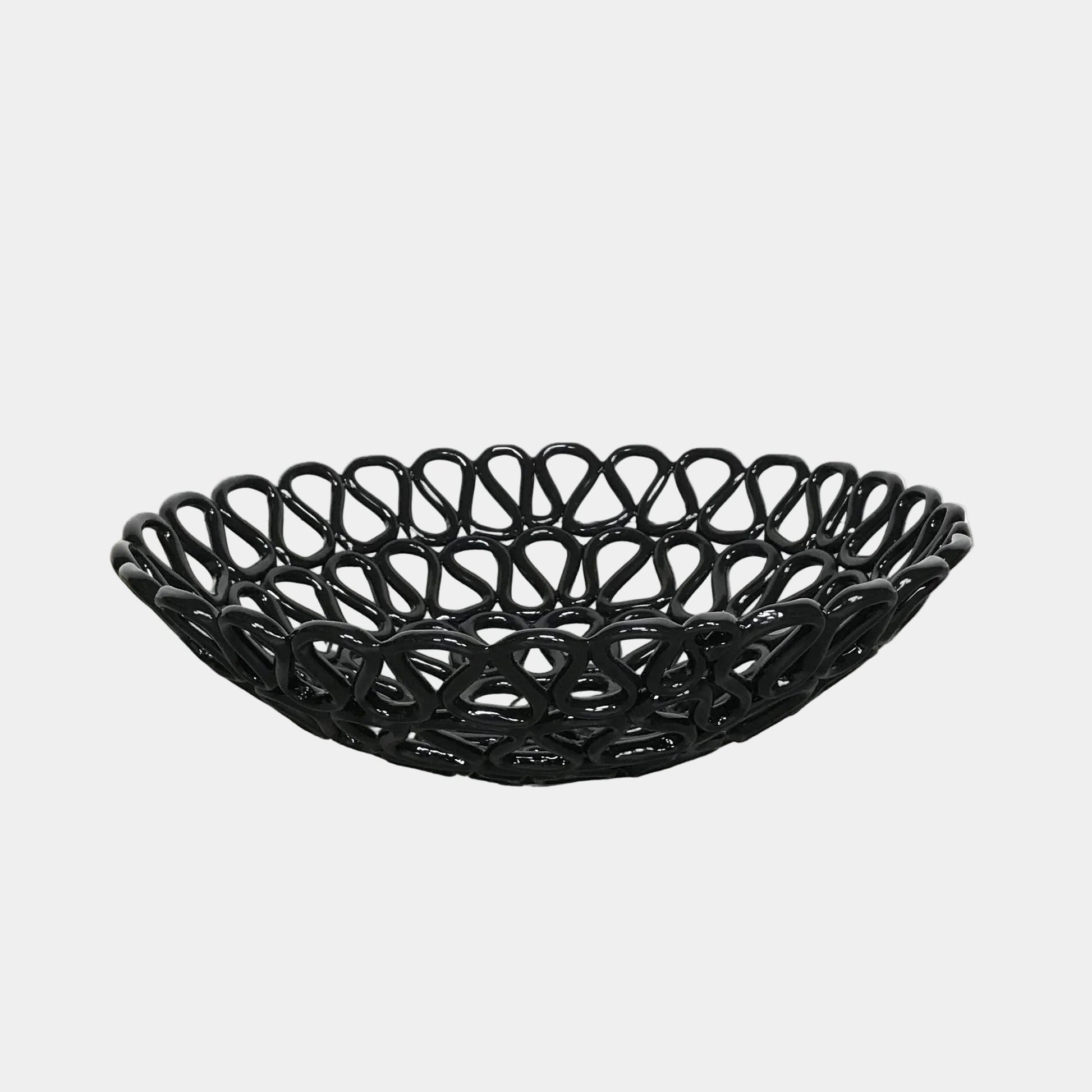 A Tom Dixon Fresh Fat Bowl in black with an intricate weave rests on a concrete floor, set against a simple white backdrop.