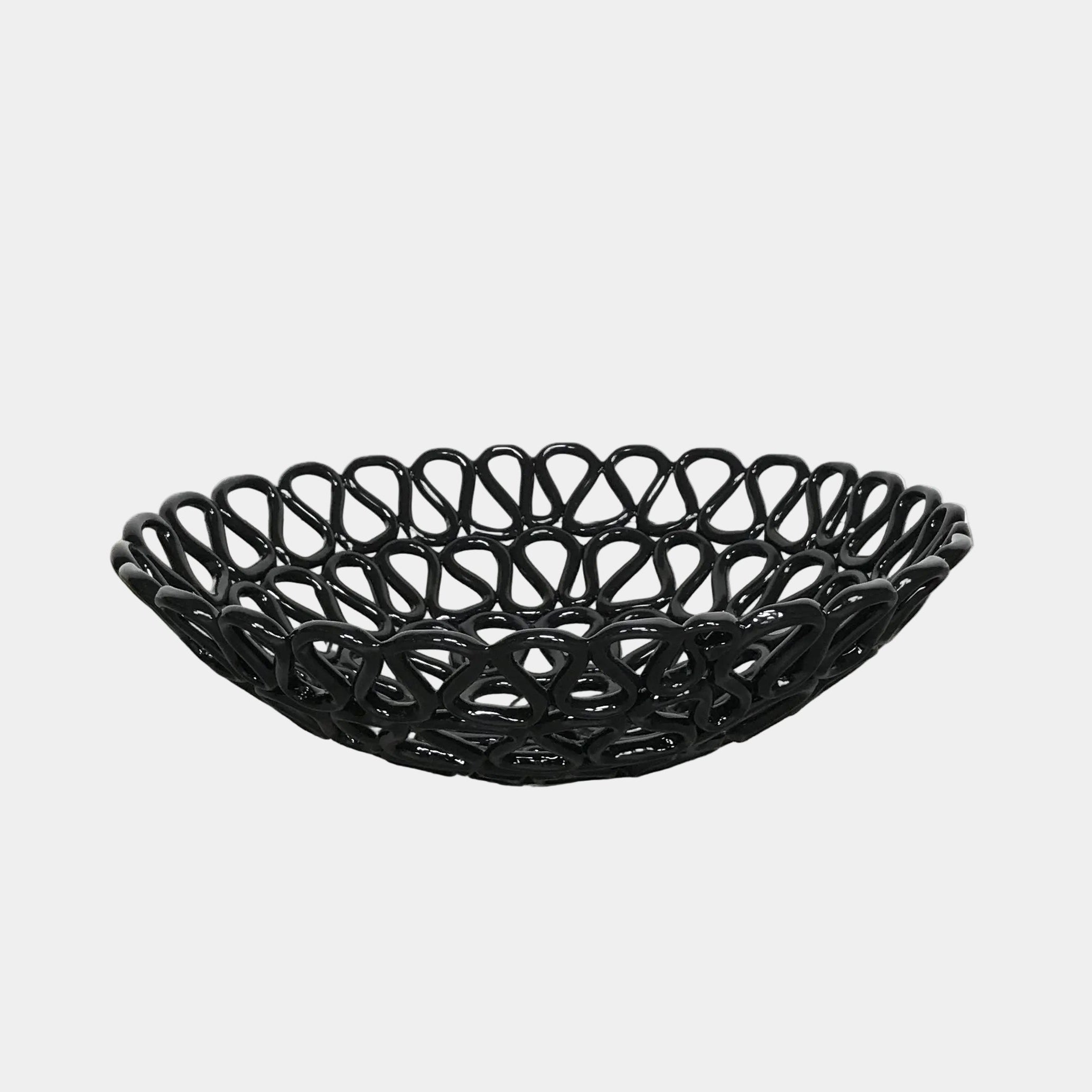 A Tom Dixon Fresh Fat Bowl in black with an intricate weave rests on a concrete floor, set against a simple white backdrop.