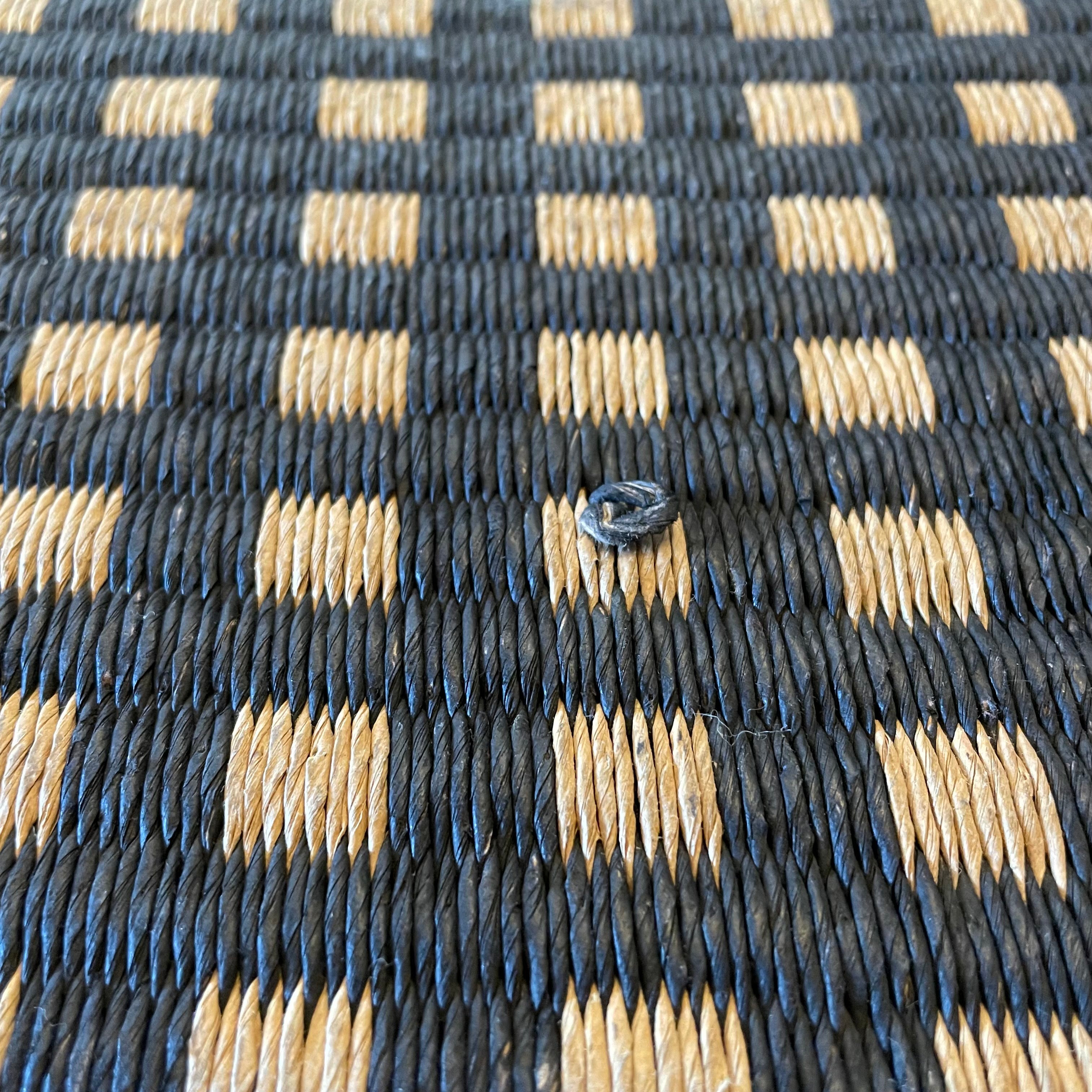 An indoor/outdoor Woodnotes City Rug with cozy detail, in black and tan, on a white surface.