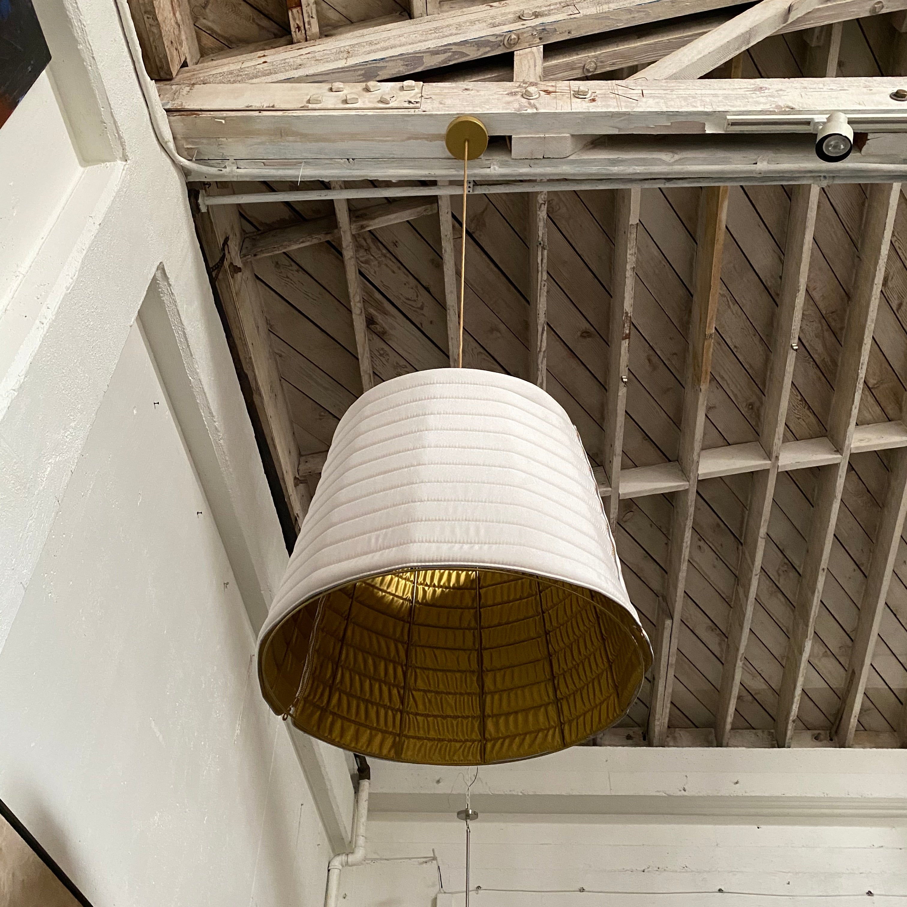 A modern suspension light featuring a white textured shade and a golden interior, suspended by a slender gold chain from Italian Vintage Ligne Roset Pharaoh Pendant.
