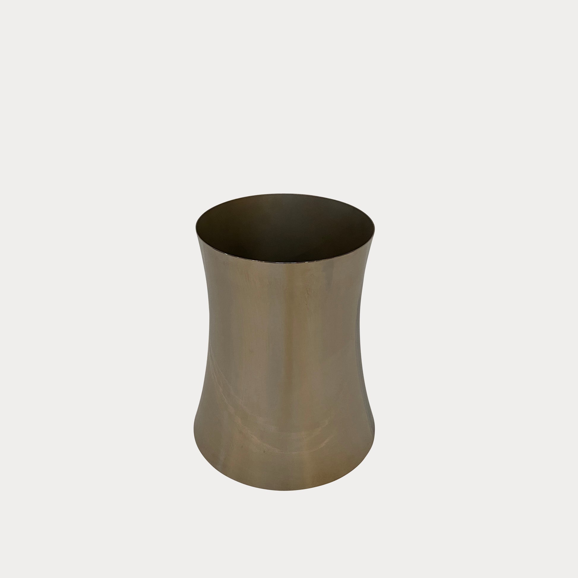 The Zubazuba Vessel by Leo Aerts, from Alinea Design Objects, is crafted from polished stainless steel with a subtly concave middle design. It stands elegantly upright against a simple backdrop, showcasing its versatility as both an artistic piece and a sophisticated champagne bucket.