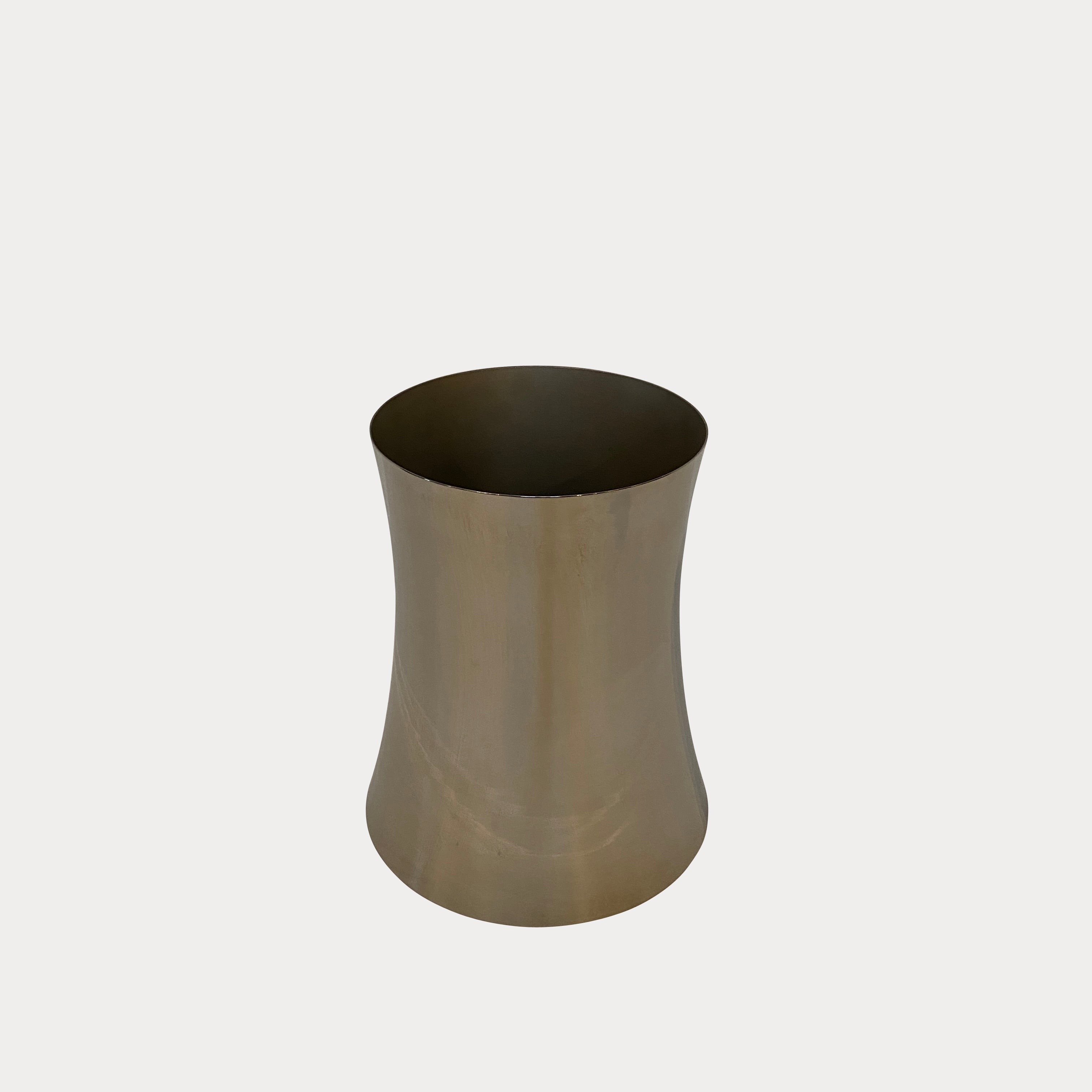 The Zubazuba Vessel by Leo Aerts, from Alinea Design Objects, is crafted from polished stainless steel with a subtly concave middle design. It stands elegantly upright against a simple backdrop, showcasing its versatility as both an artistic piece and a sophisticated champagne bucket.