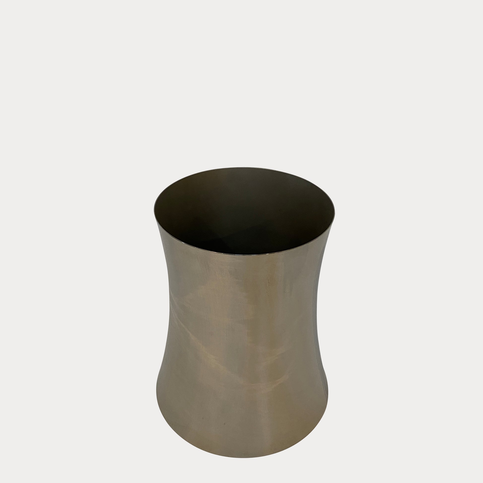 The Zubazuba Vessel by Leo Aerts, from Alinea Design Objects, is crafted from polished stainless steel with a subtly concave middle design. It stands elegantly upright against a simple backdrop, showcasing its versatility as both an artistic piece and a sophisticated champagne bucket.